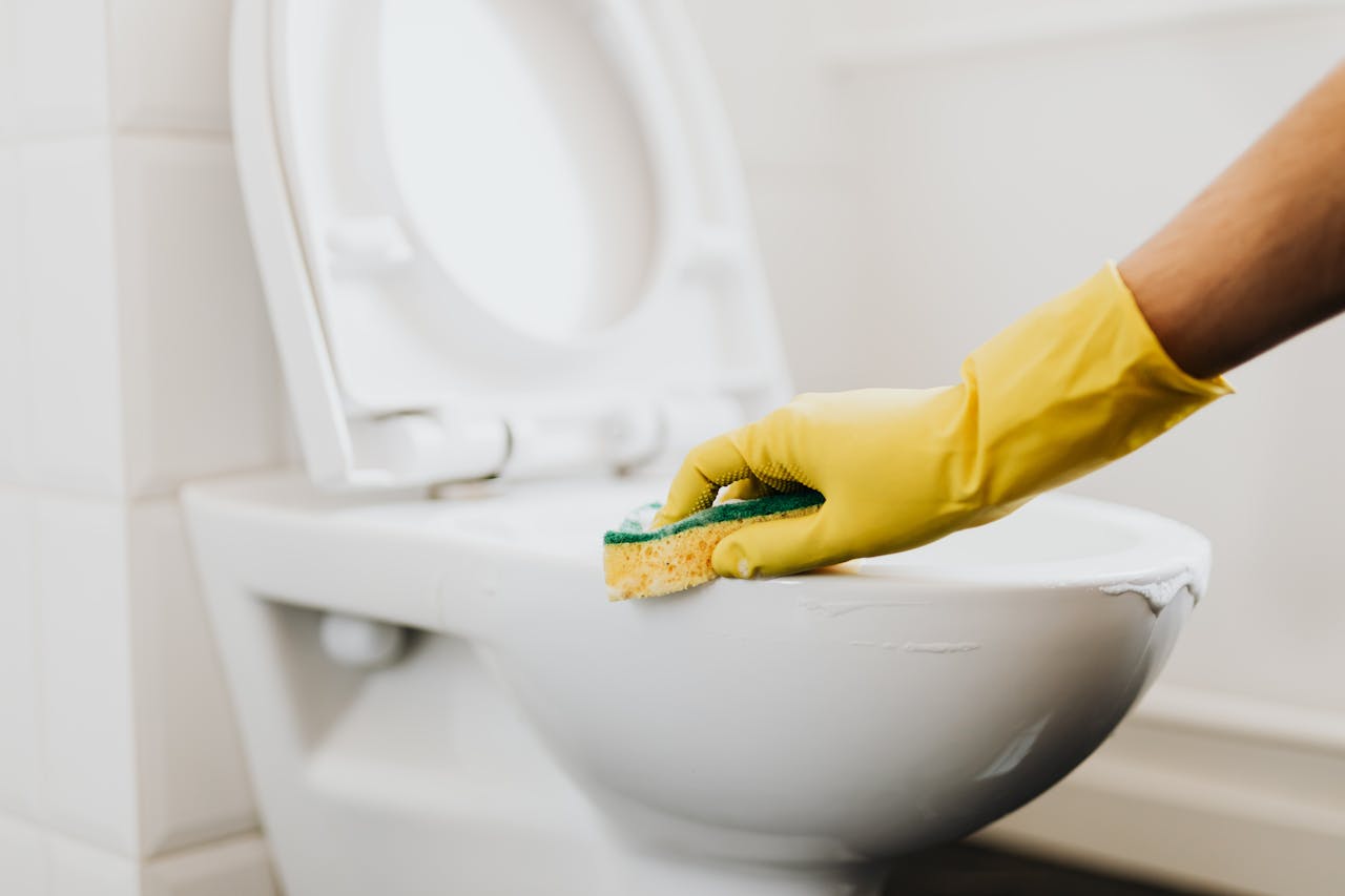 A close-up of a hand in a yellow glove cleaning a toilet with a sponge, promoting hygiene.